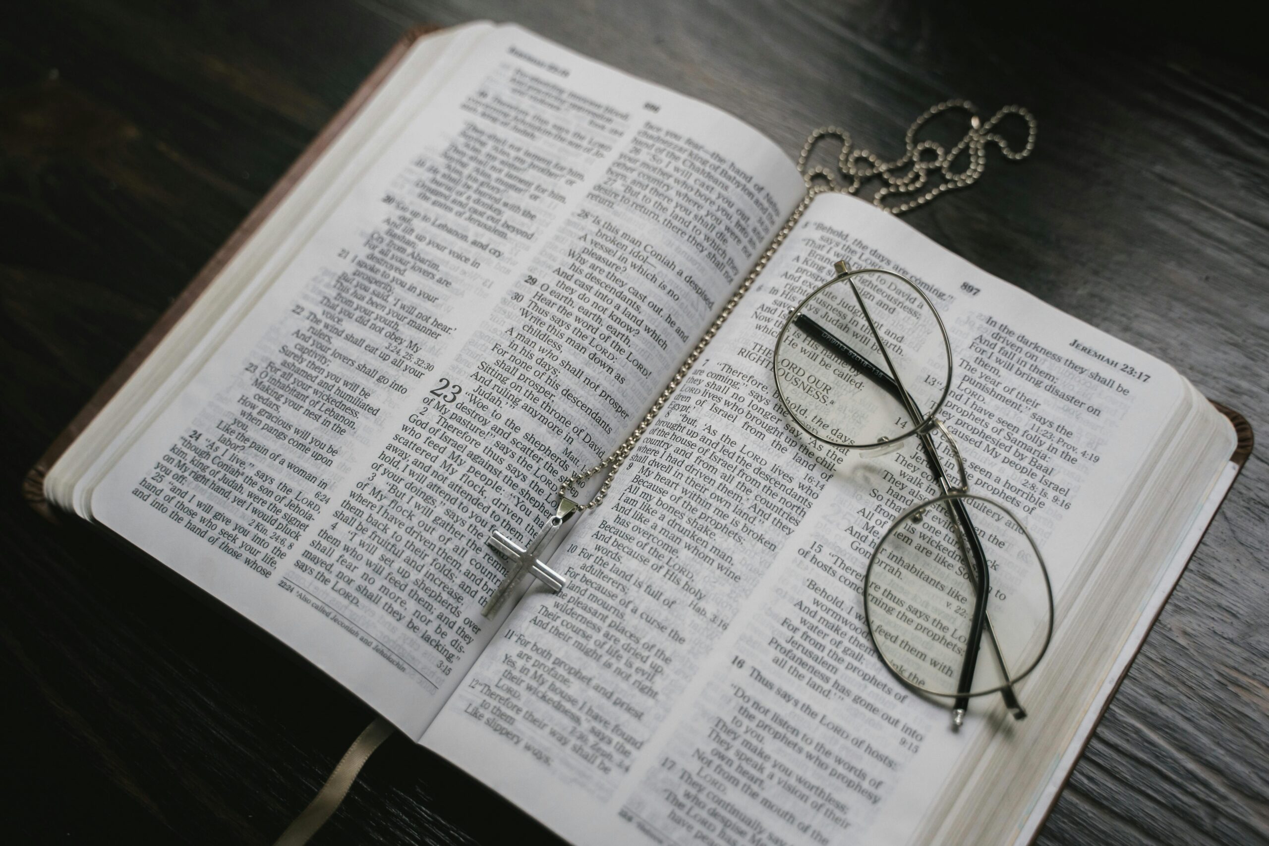 An open Bible with eyeglasses and a cross necklace resting on its pages, symbolizing faith and reflection.