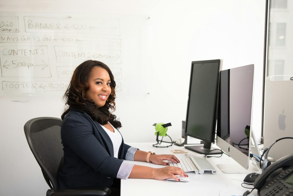 Confident businesswoman seated at her desk in an office, typing on a computer.